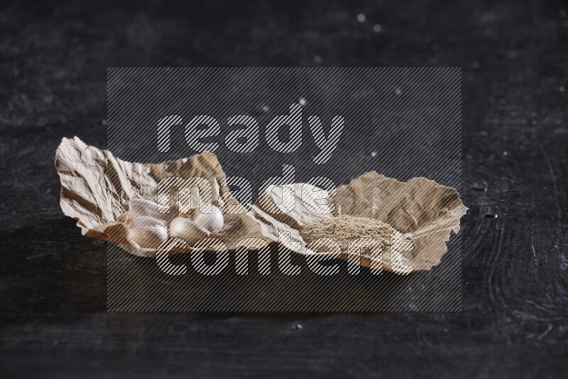 2 crumpled piece of paper full of garlic cloves and powder on a textured black flooring