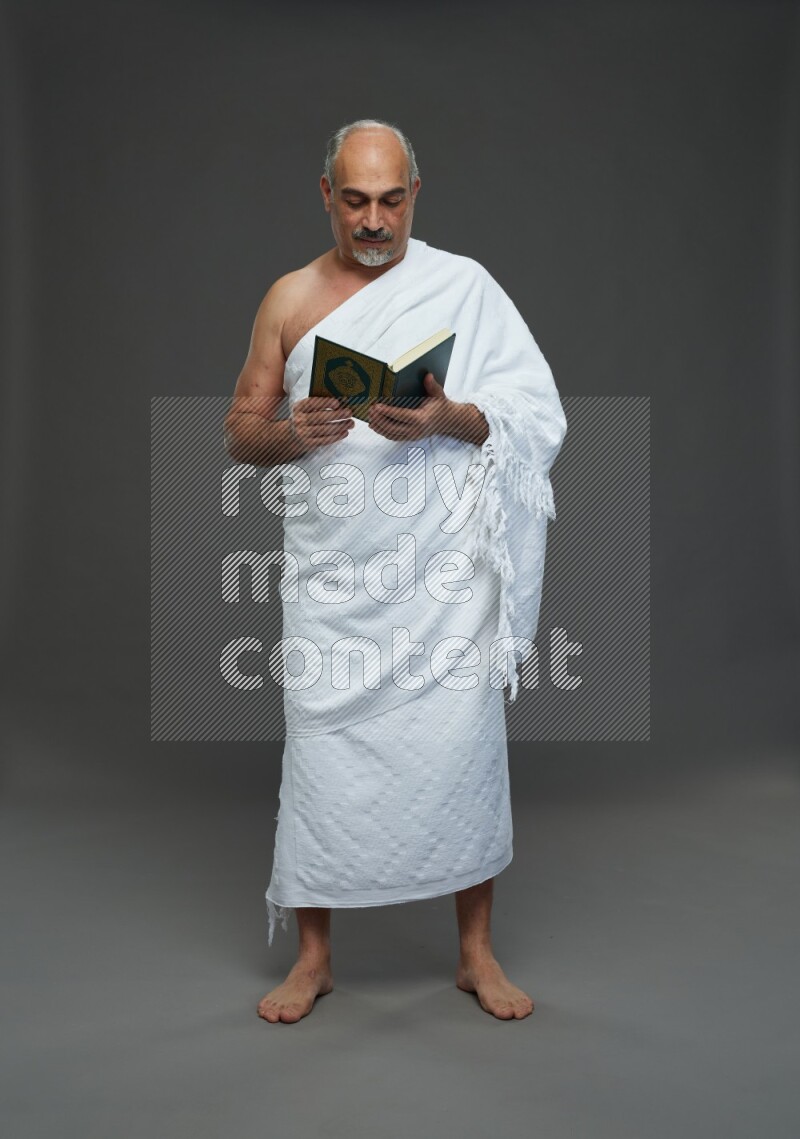 A man wearing Ehram Standing reading quran on gray background