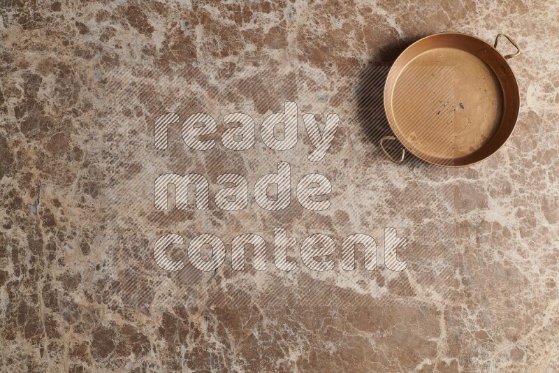 A small copper pan on beige marble background
