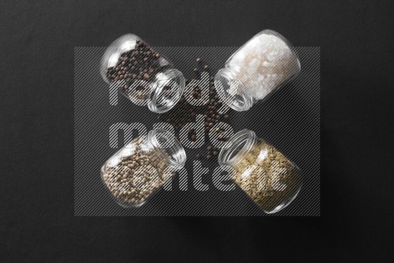 4 glass spice jars full of salt, black peppers, white peppers and cumin on black flooring