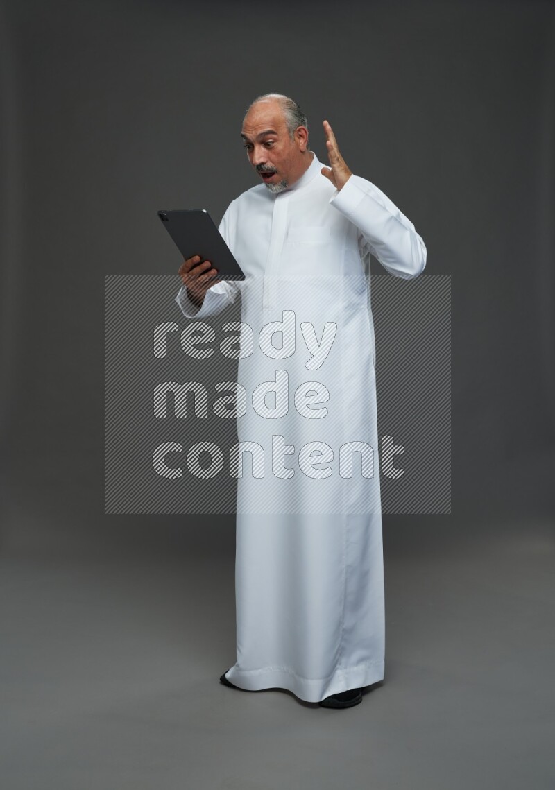 Saudi man without shomag Standing working on tablet on gray background