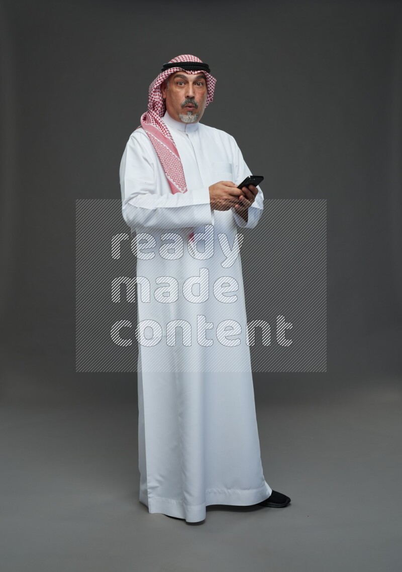Saudi man with shomag Standing texting on phone on gray background