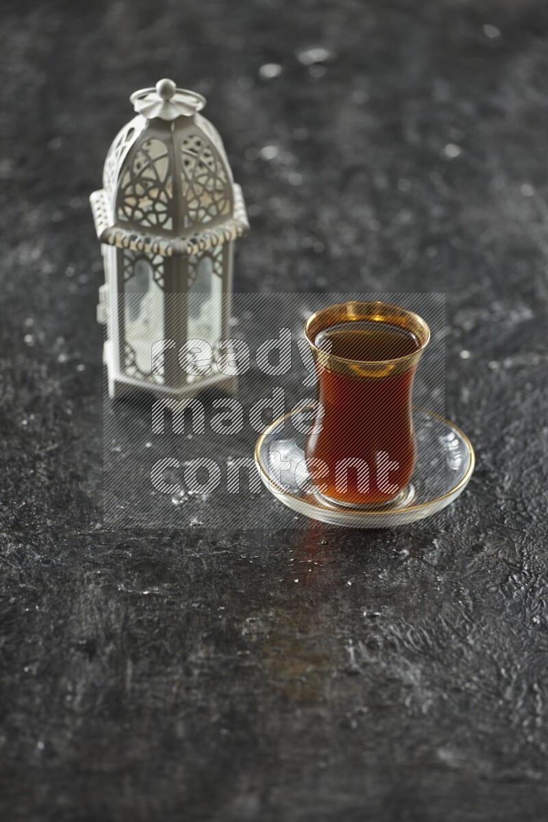 A white lantern with different drinks, dates, nuts, prayer beads and quran on textured black background
