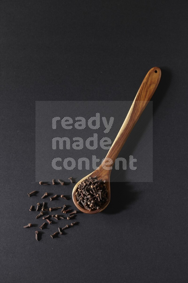 A wooden ladle full of whole cloves on a black flooring