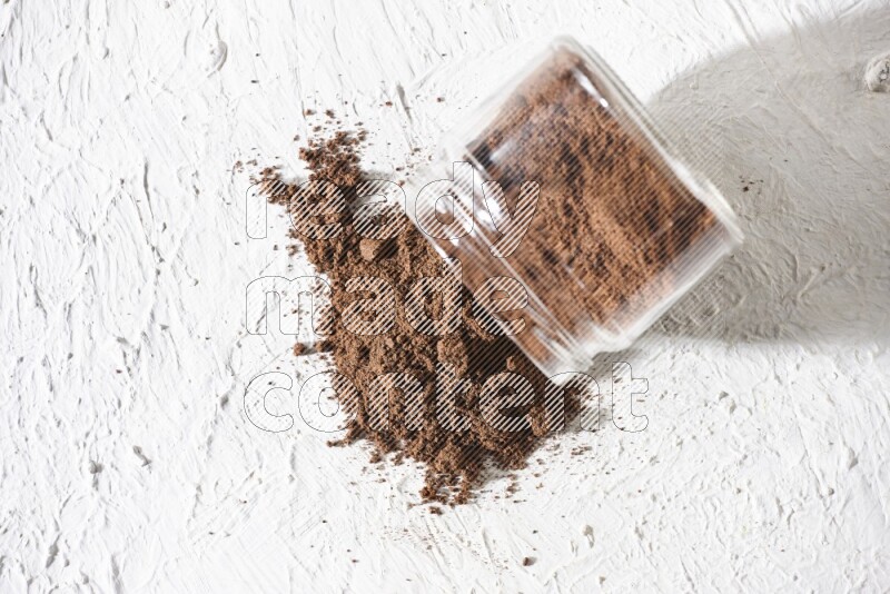 A flipped glass jar full of cloves powder on a textured white flooring