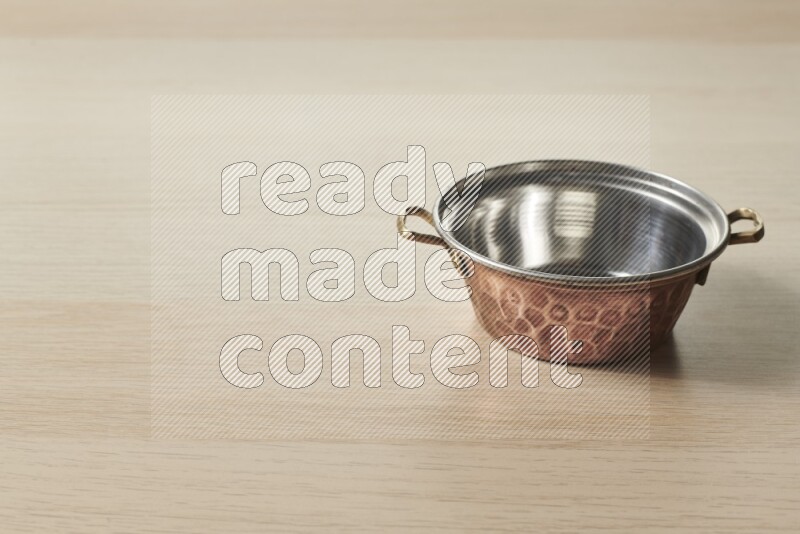 A small copper pot on light wooden background