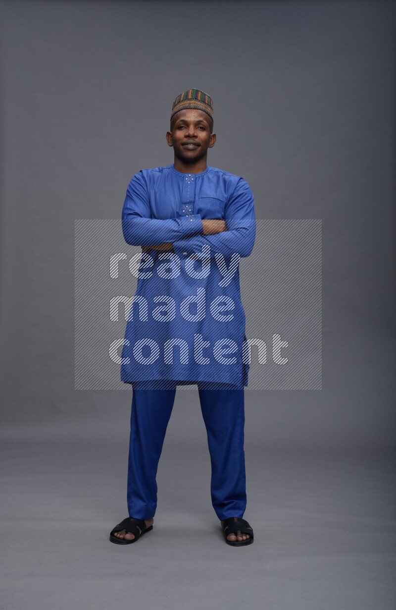 Man wearing Nigerian outfit standing with crossed arms on gray background