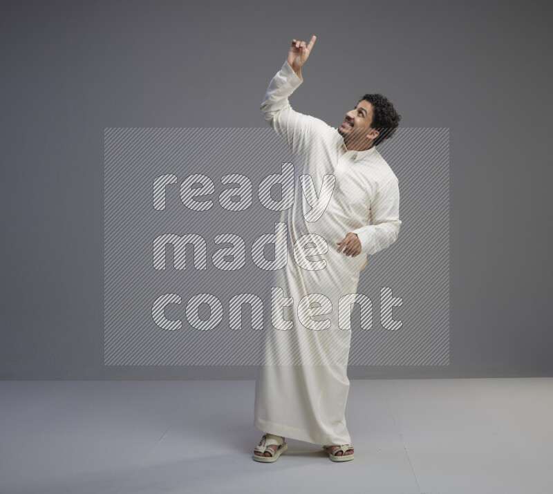 A Saudi man standing wearing thob interacting with the camera on gray background