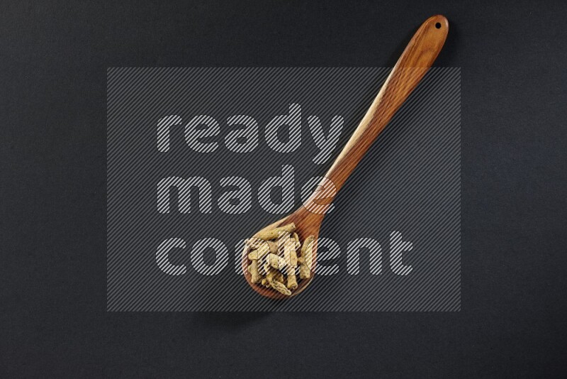 A wooden ladle full of dried turmeric fingers on black flooring