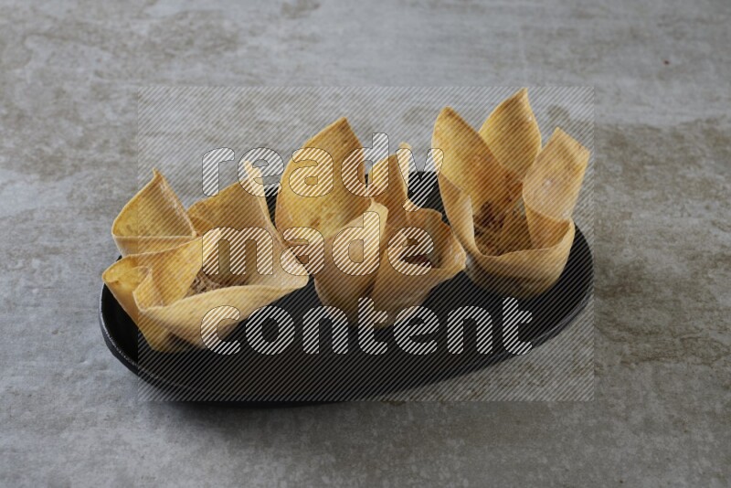 wonton cups on oval black ceramic plate on grey textured counter top