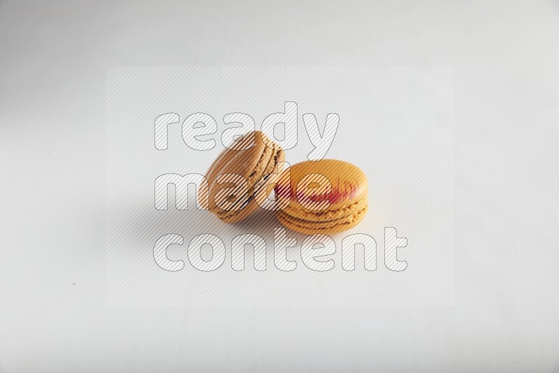 45º Shot of of two assorted Brown Irish Cream, and Orange Exotic macarons on white background