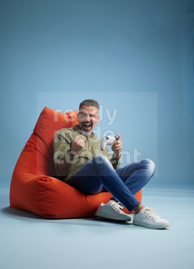 A man sitting on an orange beanbag and gaming with joystick