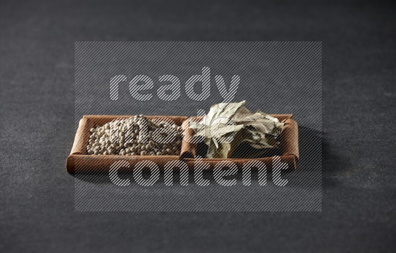 مربعان من أعواد القرفة ممتلئان بحبوب الفلفل الأبيض وأوراق الغار علي خلفية سوداء