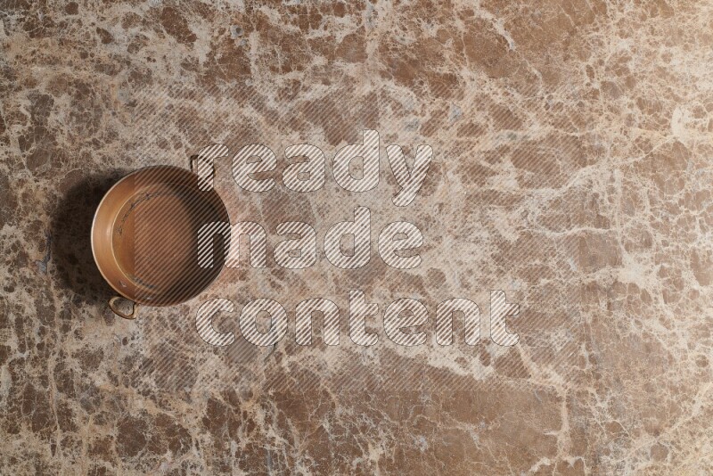 A small copper pan on beige marble background