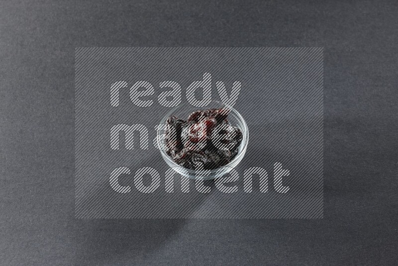 A glass bowl full of dried plums on a black background in different angles