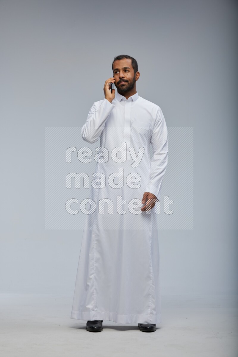 Saudi man wearing Thob standing talking on phone on Gray background