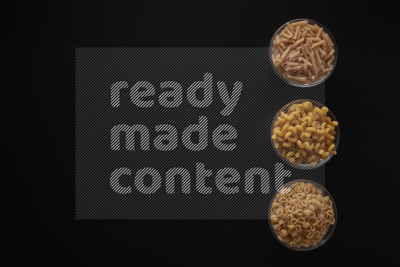 Different pasta types in 3 glass bowls on black background