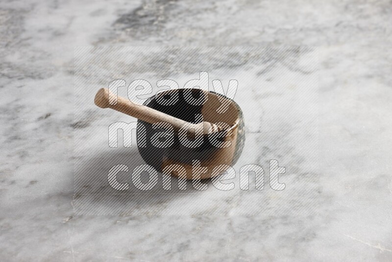 Multicolored pottery bowl with wooden honey dipper in it on grey marble background
