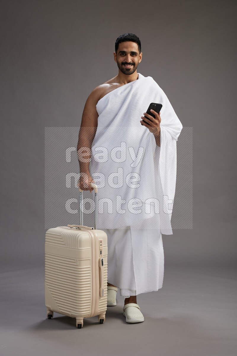 A man wearing Ehram Standing holding traveling bag on gray background