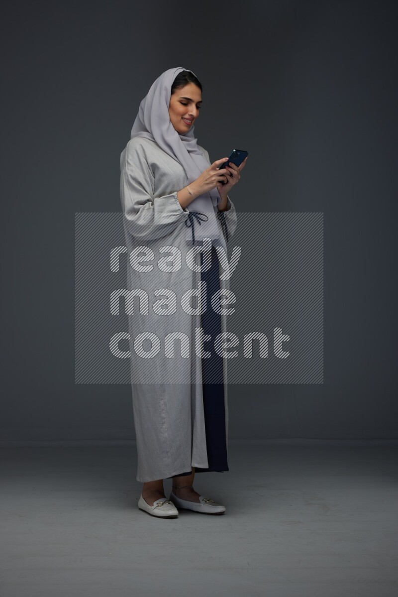 A Saudi woman Texting wearing Grey Abaya on a grey background