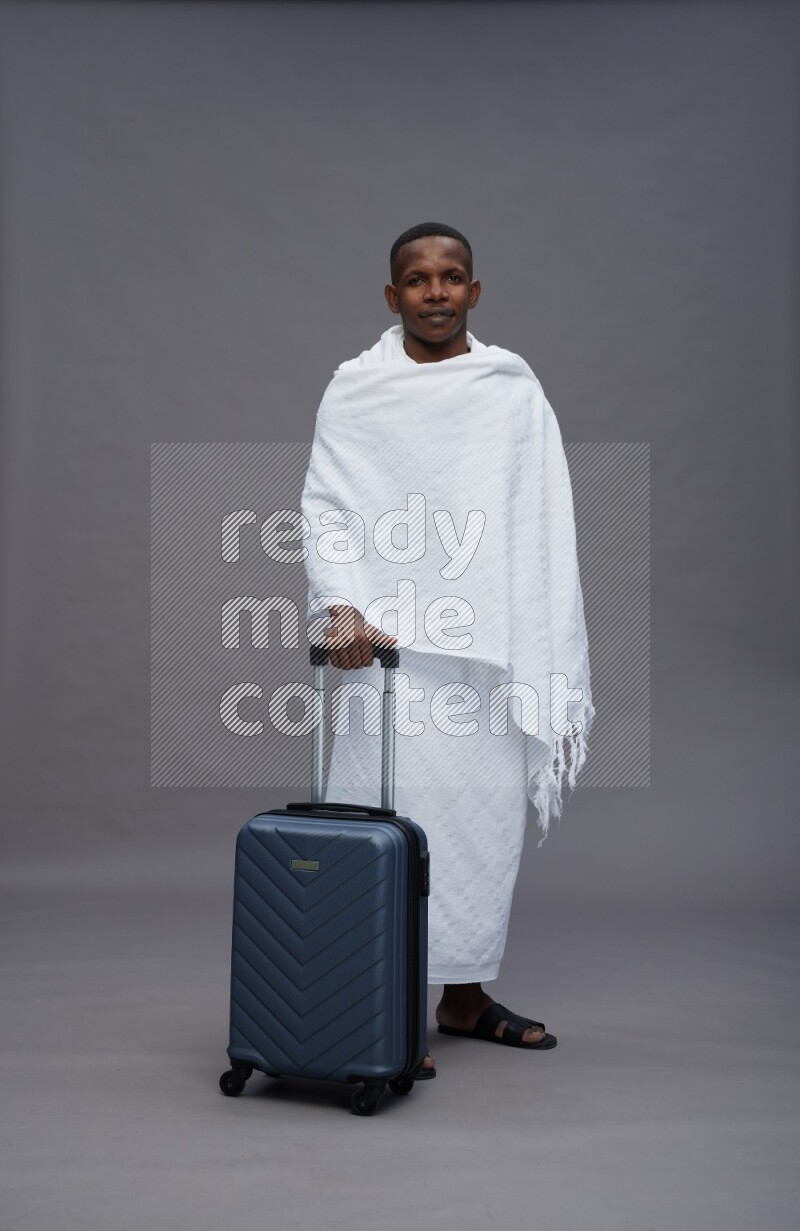 A man wearing Ehram Standing holding traveling bag on gray background