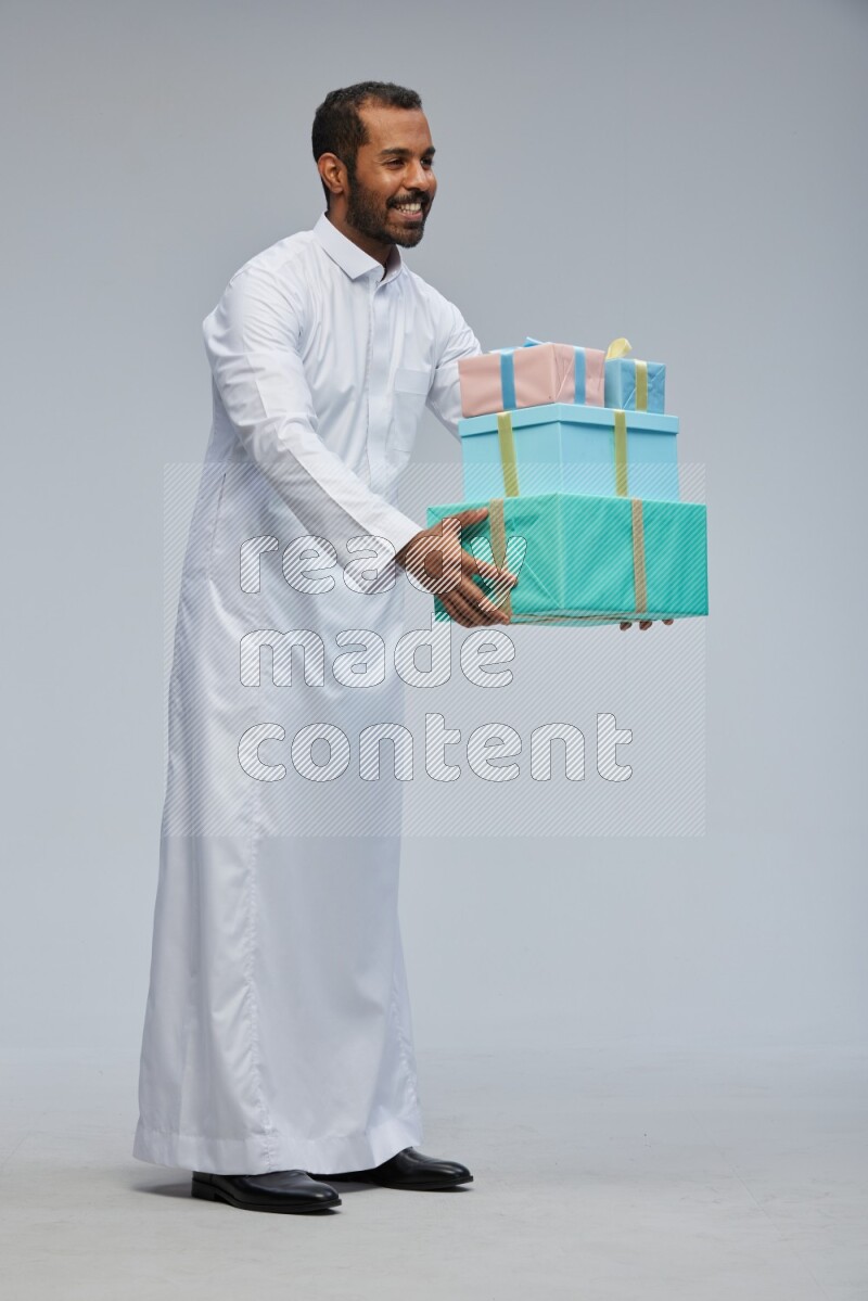 Saudi man Wearing thob standing holding gift box on Gray background