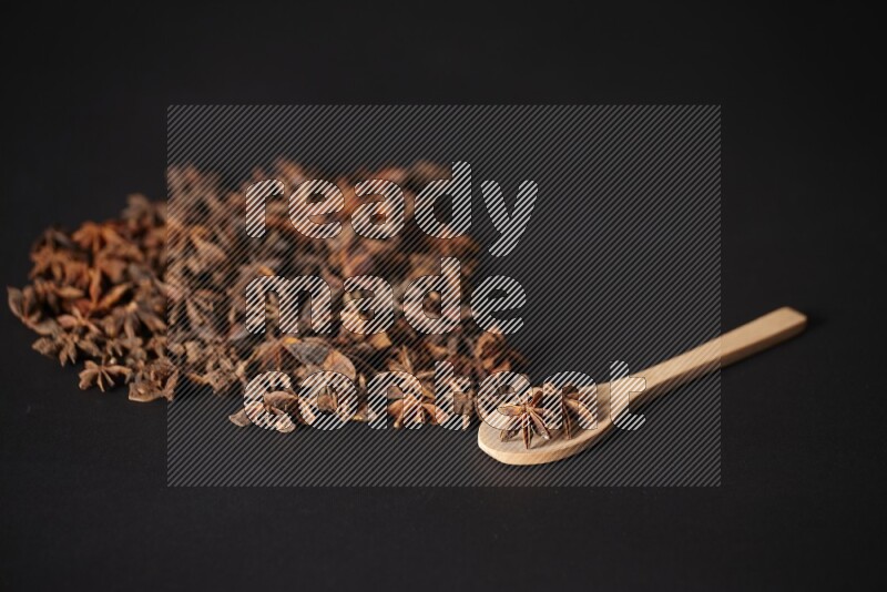 اليانسون النجمي في ملعقة خشبية ومتناثر على أرضية سوداء