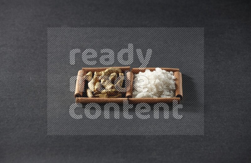 مربعان من أعواد القرفة ممتلئان بالملح الأبيض وأصابع الكركم علي خلفية سوداء