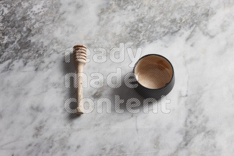 Multicolored pottery bowl with wooden honey dipper on the side on grey marble background