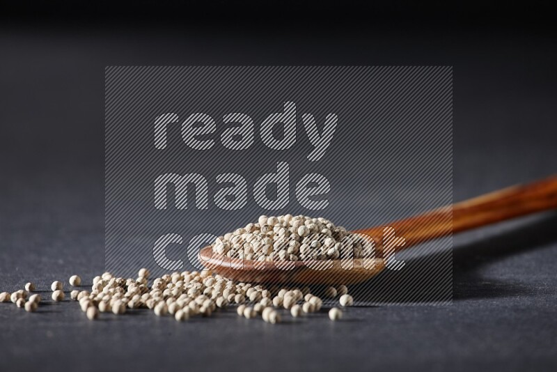 A wooden ladle full of white pepper beads on black flooring