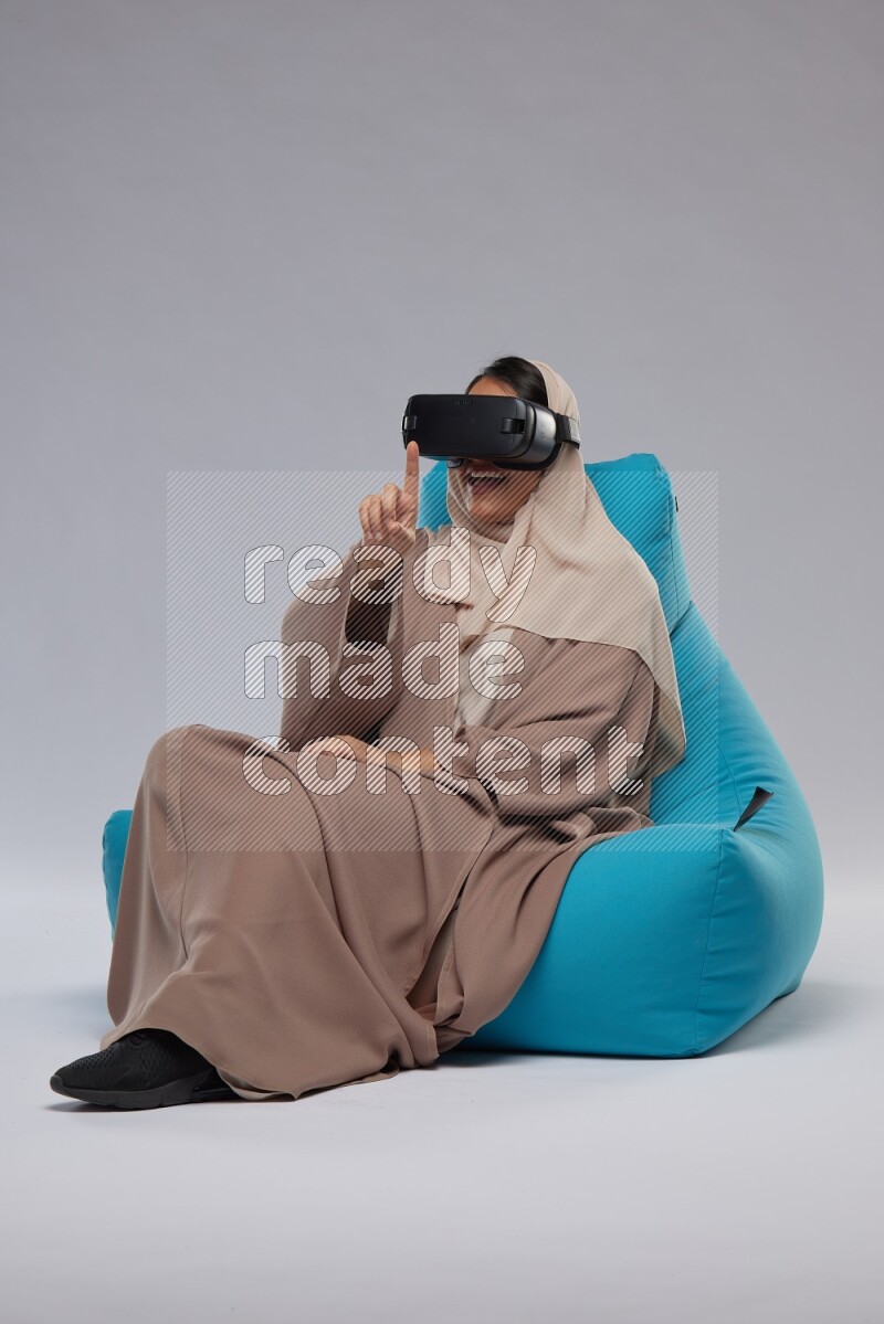 A Saudi woman sitting on a blue beanbag and gaming with VR