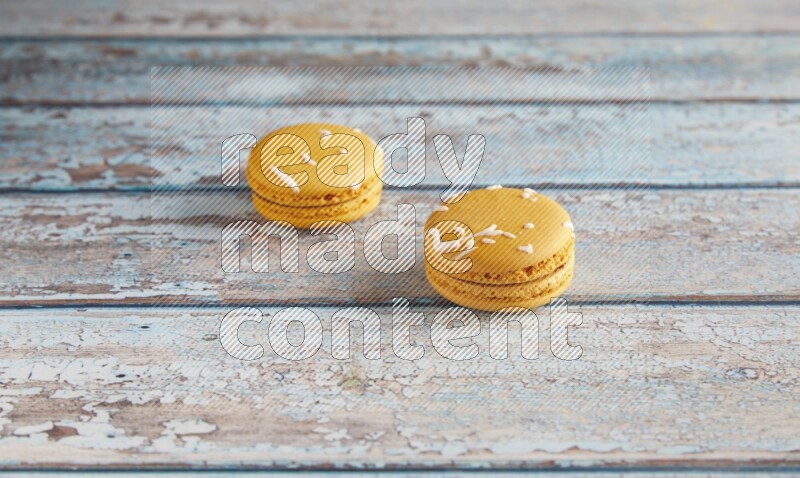 45º Shot of two Yellow Piña Colada macarons on light blue wooden background