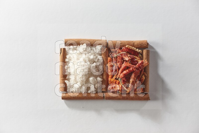 2 squares of cinnamon sticks full of dried red chilis and white salt on white flooring