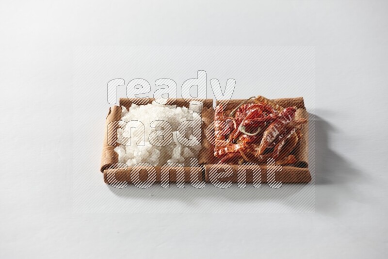 2 squares of cinnamon sticks full of dried red chilis and white salt on white flooring