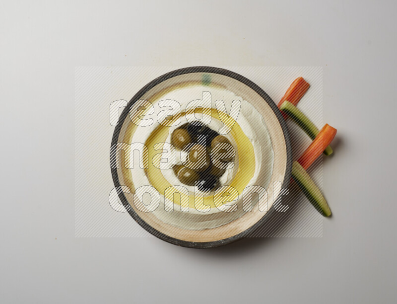 Lebnah garnished with whole black olives in a pottery plate on a white background