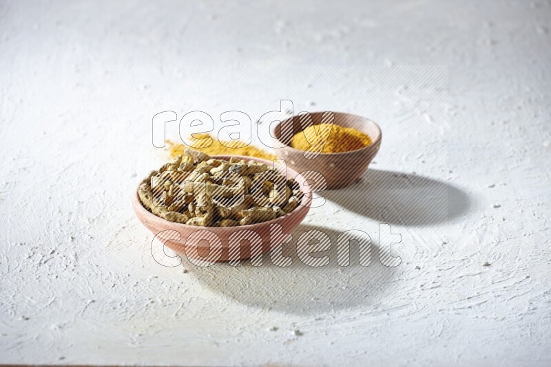 وعاءان خشبيان، أحدهما ممتلئ ببودرة الكركم والآخر بأصابع الكركم المجففة، على خلفية بيضاء