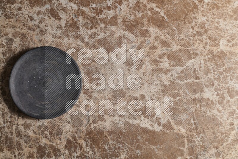 A circular black pottery plate on beige marble background