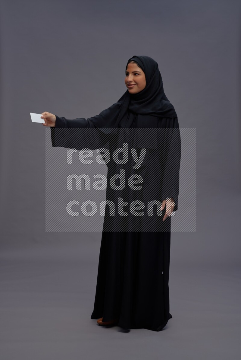 Saudi woman wearing Abaya standing holding ATM card on gray background