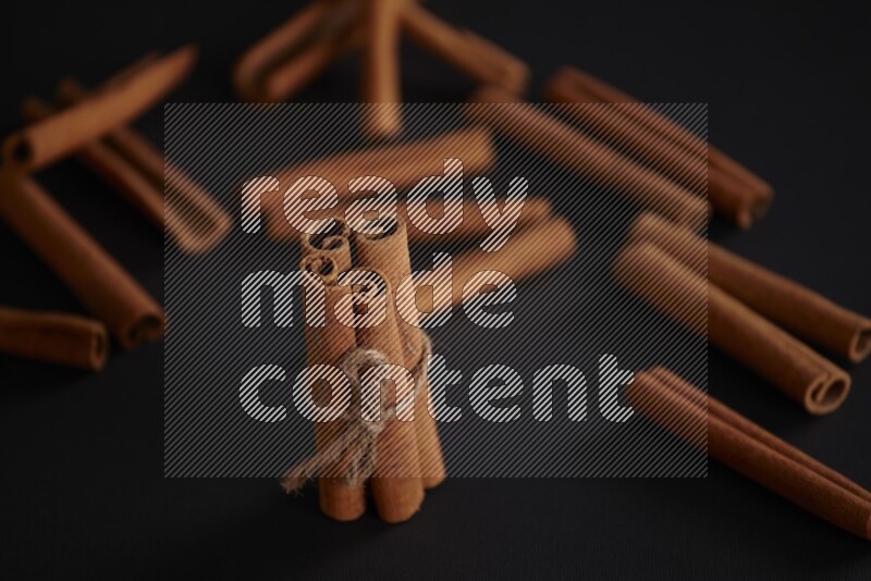 4 Cinnamon sticks stacked and bounded with more sticks in the background on black flooring