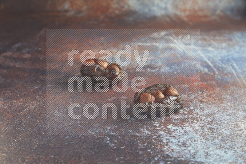 two hazelnut stuffed madjoul dates on a rustic reddish background
