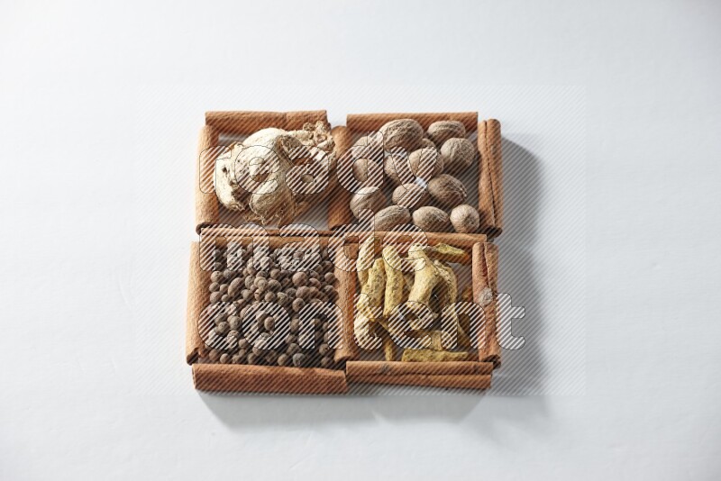 4 مربعات من أعواد القرفة ممتلئة بجوزة الطيب والزنجبيل المجفف وأصابع الكركم وبهار الفلفل الحلو على أرضية بيضاء