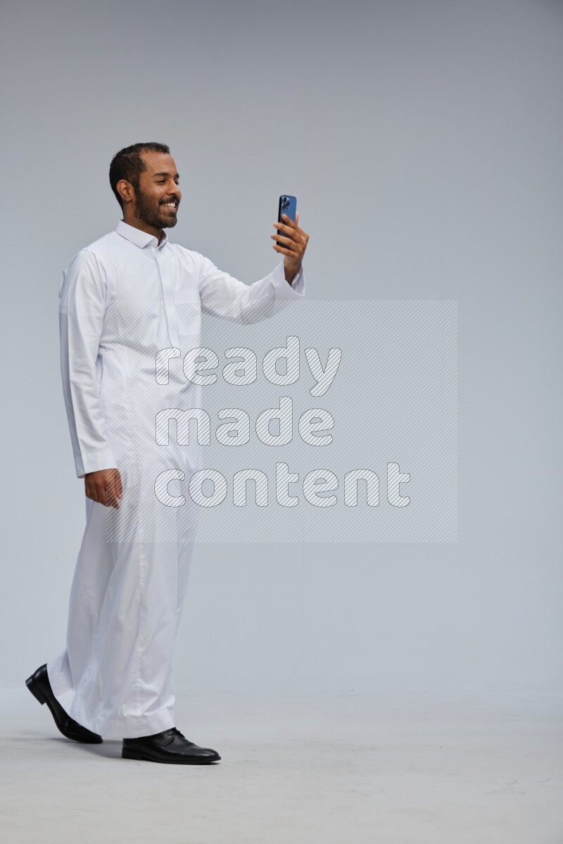 Saudi man wearing Thob standing taking selfie on Gray background