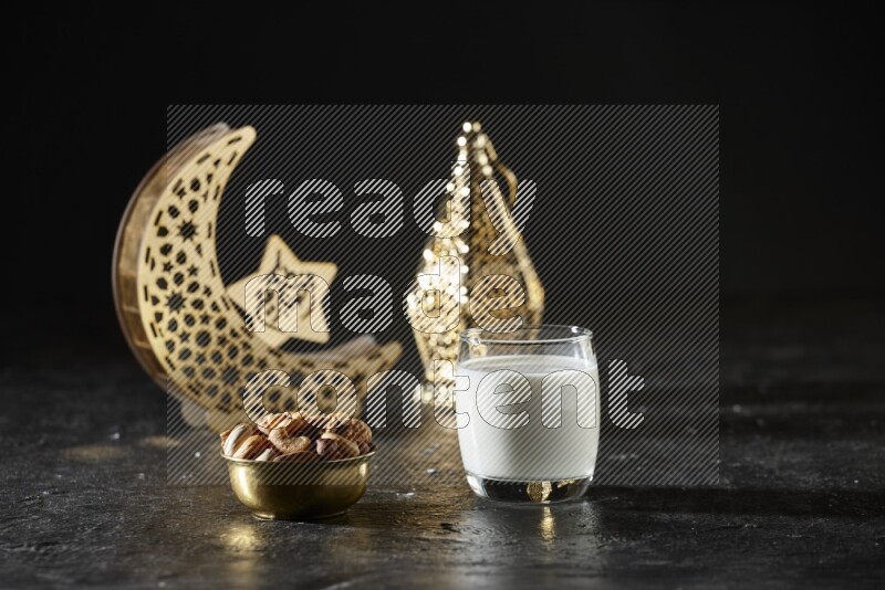 Nuts in a metal bowl with milk beside golden lanterns in a dark setup