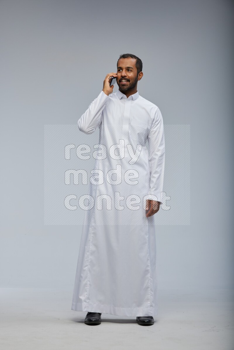 Saudi man wearing Thob standing talking on phone on Gray background