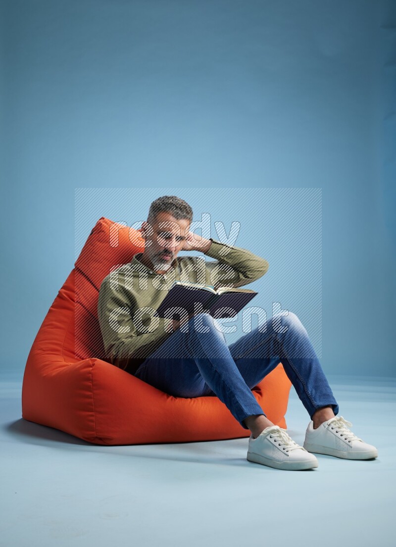 A man sitting on an orange beanbag and reading a book