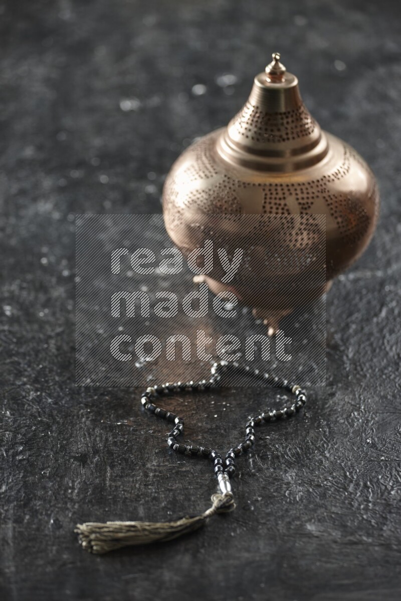 A golden lantern with different drinks, dates, nuts, prayer beads and quran on textured black background
