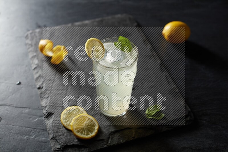 A glass of lemon juice with a lemon slice on black background