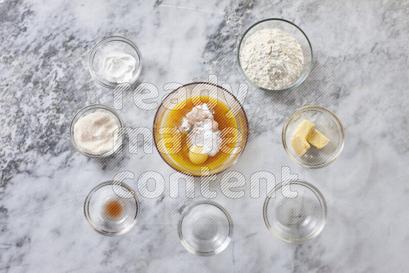 كوكيز خطوة بخطوة بمكوناتها، الدقيق، الزبدة، السكر البني، البيض، الفانيليا، السكر الأبيض، رقائق الشوكولاتة وصودا الخبز على خلفية رخام رمادي