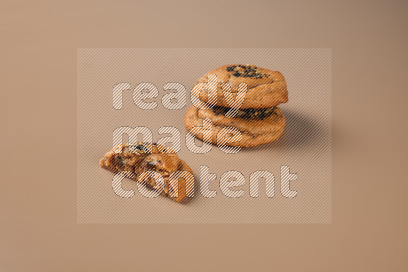 Two Hasawi cookies field of date and decorated by black seed and anise grain with another one cut in half on a brown background