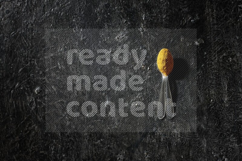 ملعقتان معدنيتان ممتلئتان ببودرة الكركم على خلفية سوداء